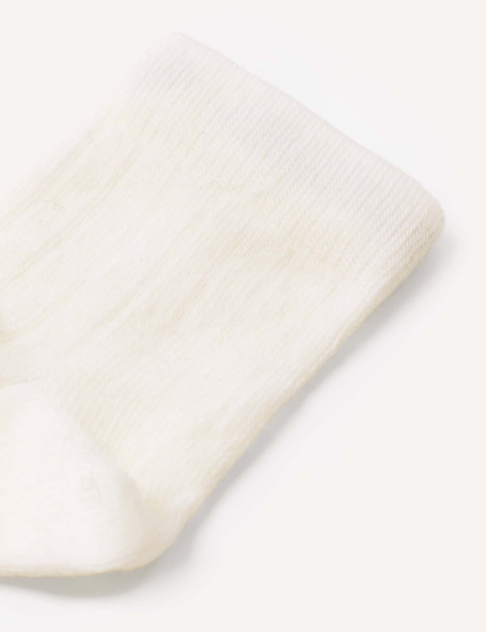 Close-up of a white, ribbed, knitted Socks – Merino Baby Light on a light background. The texture and pattern of the fabric are clearly visible, highlighting the quality craftsmanship and durability of these baby socks.