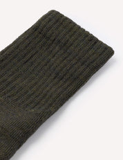 A close-up of a dark green, ribbed knit fabric—likely the cuff of the Terry Socks – Merino Kids—shown on a plain white background.