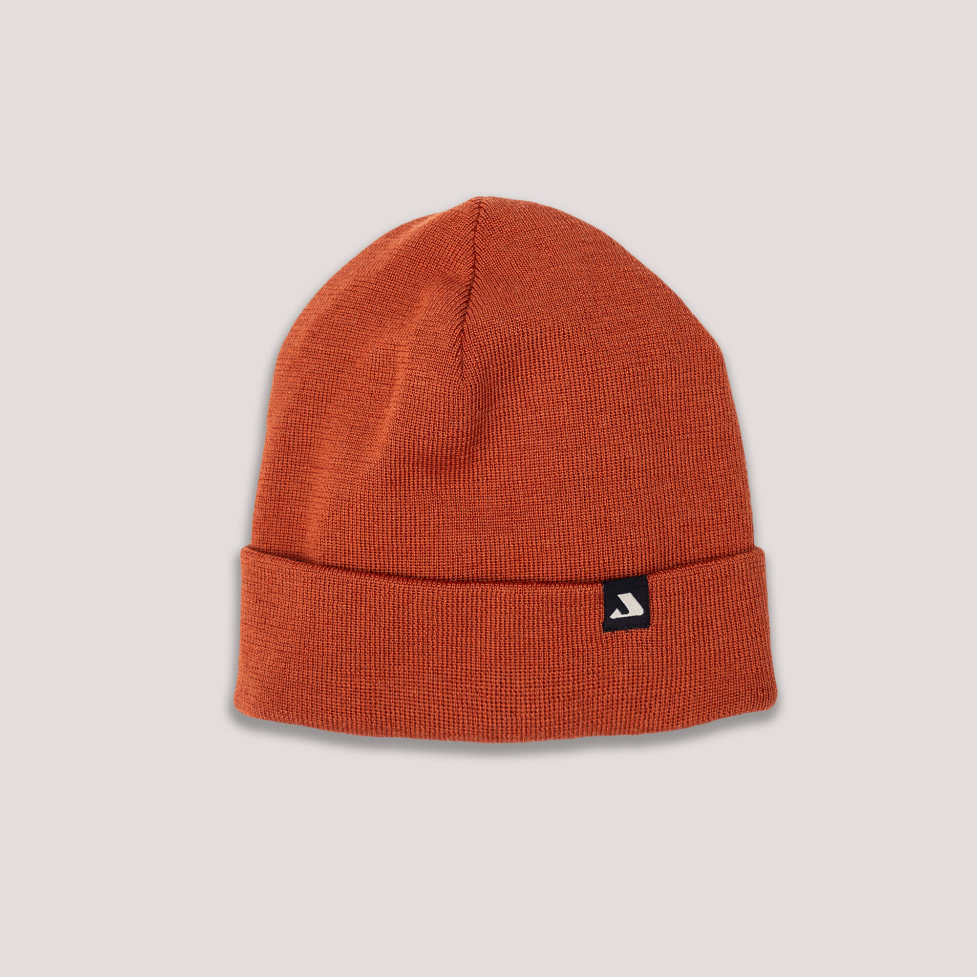 The Beanie – MeshWool is a rust-colored merino wool hat with a folded brim and a small black rectangular tag featuring a white logo, shown on a light gray background.