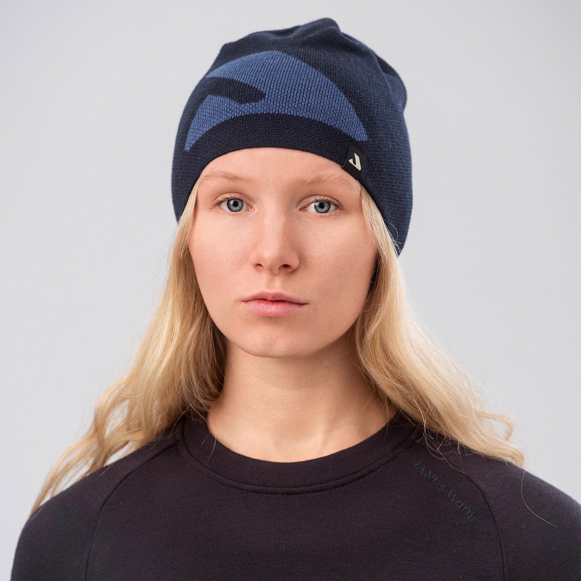 A woman with long blonde hair wears the navy Beanie – Logo, looking at the camera against a plain light gray background, showcasing its warmth and breathability.