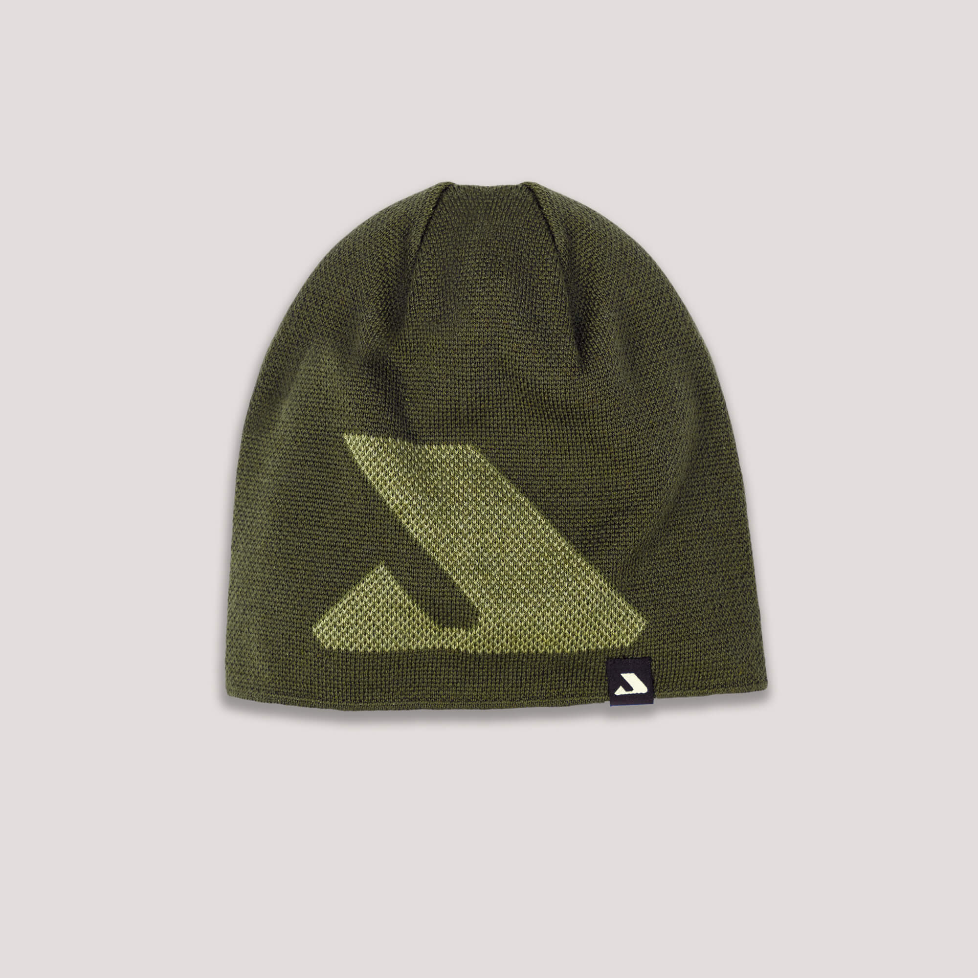 The Beanie – Logo in Forest Night features a large light green arrow design on the front and a small black tag with a white arrow logo at the edge. Made from merino wool for warmth and breathability. Set against a light pink background.