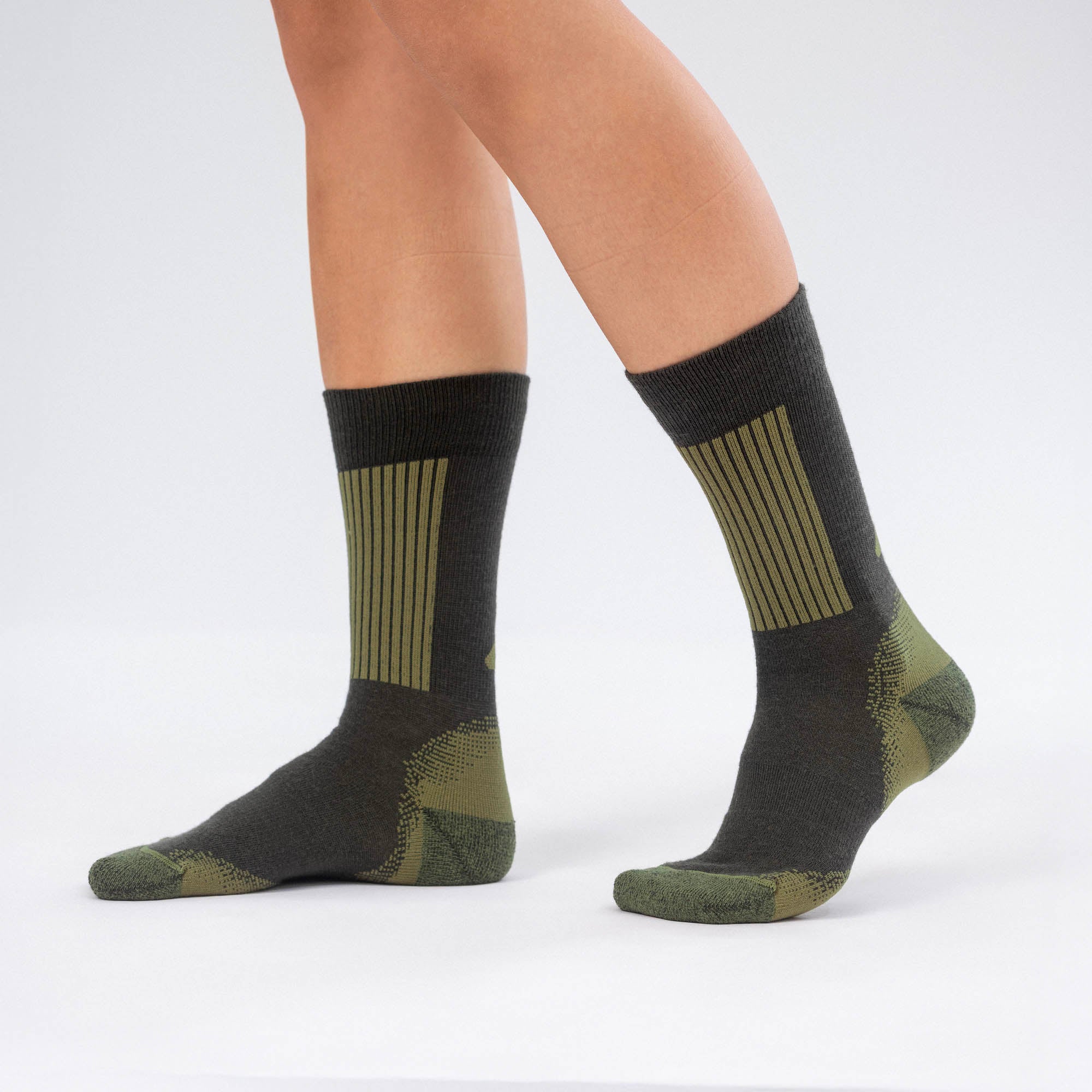 A person wearing Forest Night Socks Merino – Hiking stands on a light surface. These socks have ribbed patterns and contrasting sections on the toes, heels, and ankles for added comfort.