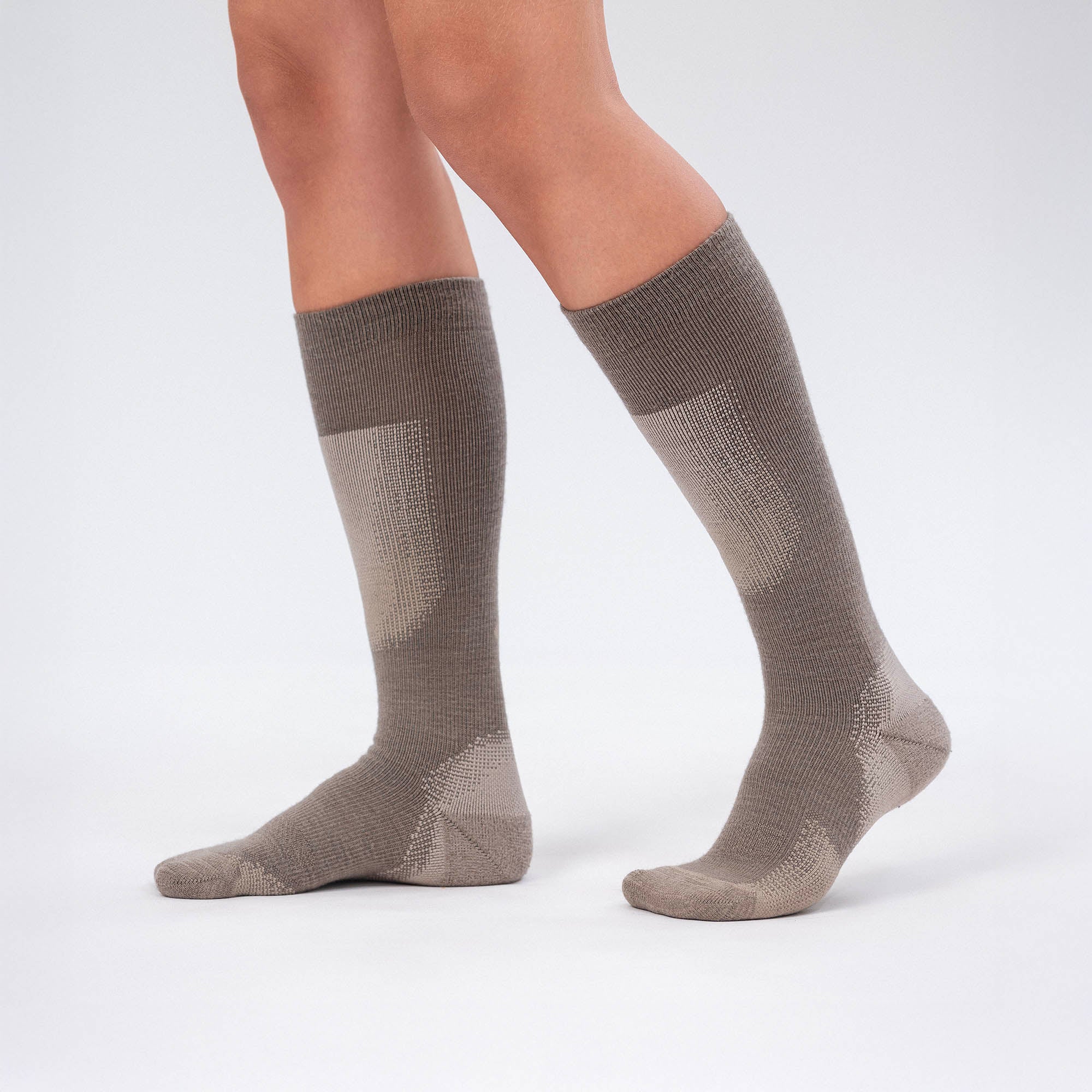 A person wears beige Socks Merino – Cross Country, known for excellent breathability, while standing against a plain light gray background.