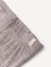 A close-up of a light brown, textured fabric with visible stitching and a small beige tag reading 100% linen attached to the edge—perfect for wearing as a comfortable base layer beneath the Leggings – Merino Baby Light.