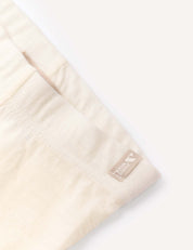 Close-up of a light beige, soft fabric garment identified as the Leggings – Merino Baby Light, featuring a small tan woven label reading 100% TENCEL LYOCELL sewn into the seam. This fabric is ideal for use as a base layer or lightweight leggings. The background is a plain, light color.