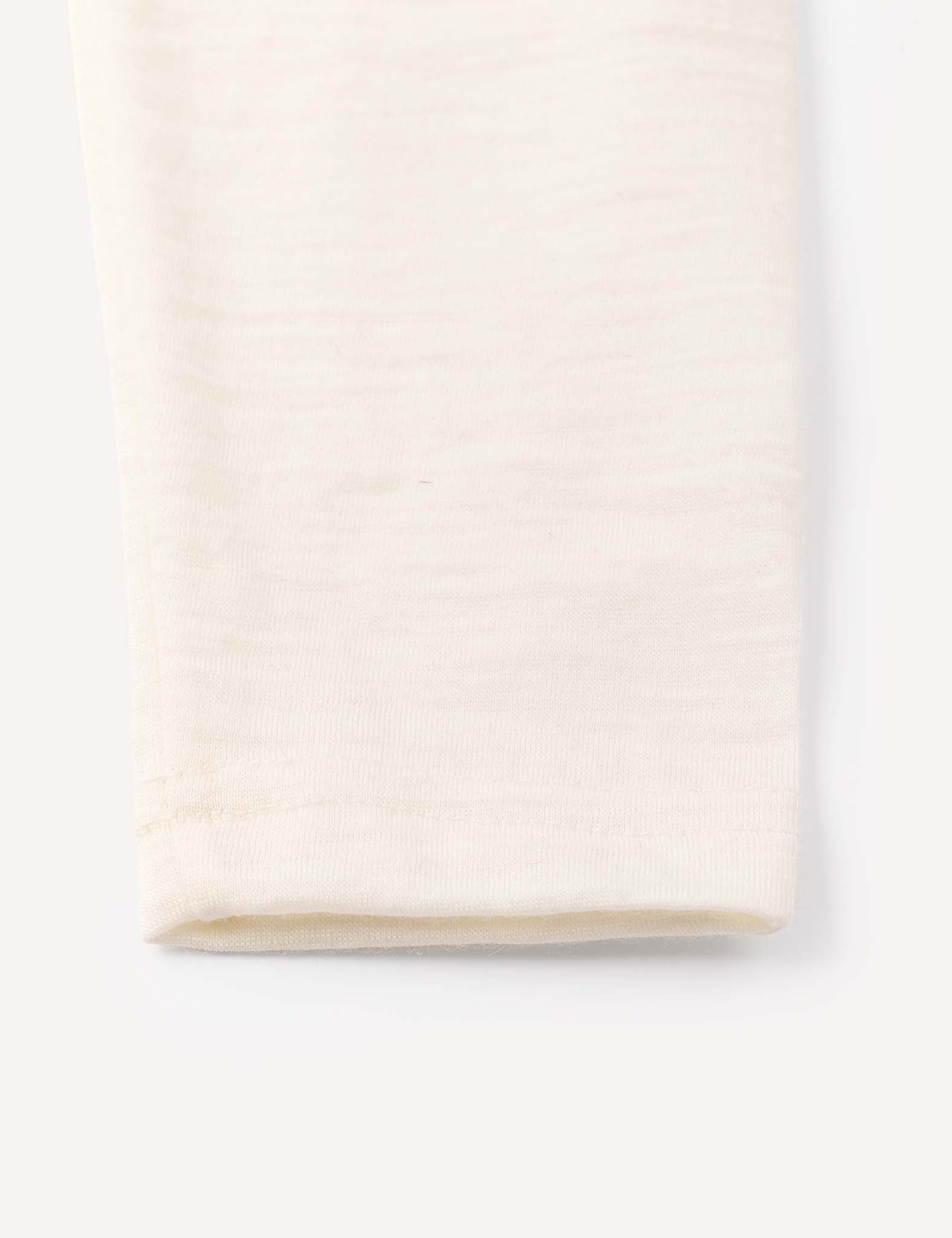 A close-up of the hem of the Leggings – Merino Baby Light in a light cream shade, set against a white background, highlights the refined simplicity and softness characteristic of these lightweight merino base layers.