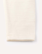 A close-up of the hem of the Leggings – Merino Baby Light in a light cream shade, set against a white background, highlights the refined simplicity and softness characteristic of these lightweight merino base layers.