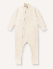 The Pyjamas – Merino Baby Light in Marshmallow is a breathable, cream-colored baby onesie designed for ultimate comfort, featuring long sleeves and legs, ribbed cuffs, and an asymmetrical front zipper running from the neck down to the left leg.