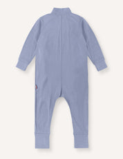 The Pyjamas – Merino Baby Light is a long-sleeve, light blue onesie shown from the back. Designed as breathable pyjamas, it features ribbed cuffs on the sleeves and legs and is finished with a small logo tag on the left side near the hip.