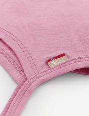 Close-up of a pink Bonnet – Merino Baby Light with visible stitching and a small beige tag featuring a red, white, and blue stripe detail. This breathable baby hat is designed for comfort and style.