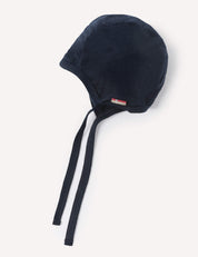 A navy Merino Baby Light bonnet with chin ties, displayed against a plain white background. A small rectangular tag with a red and white design is attached near the edge.