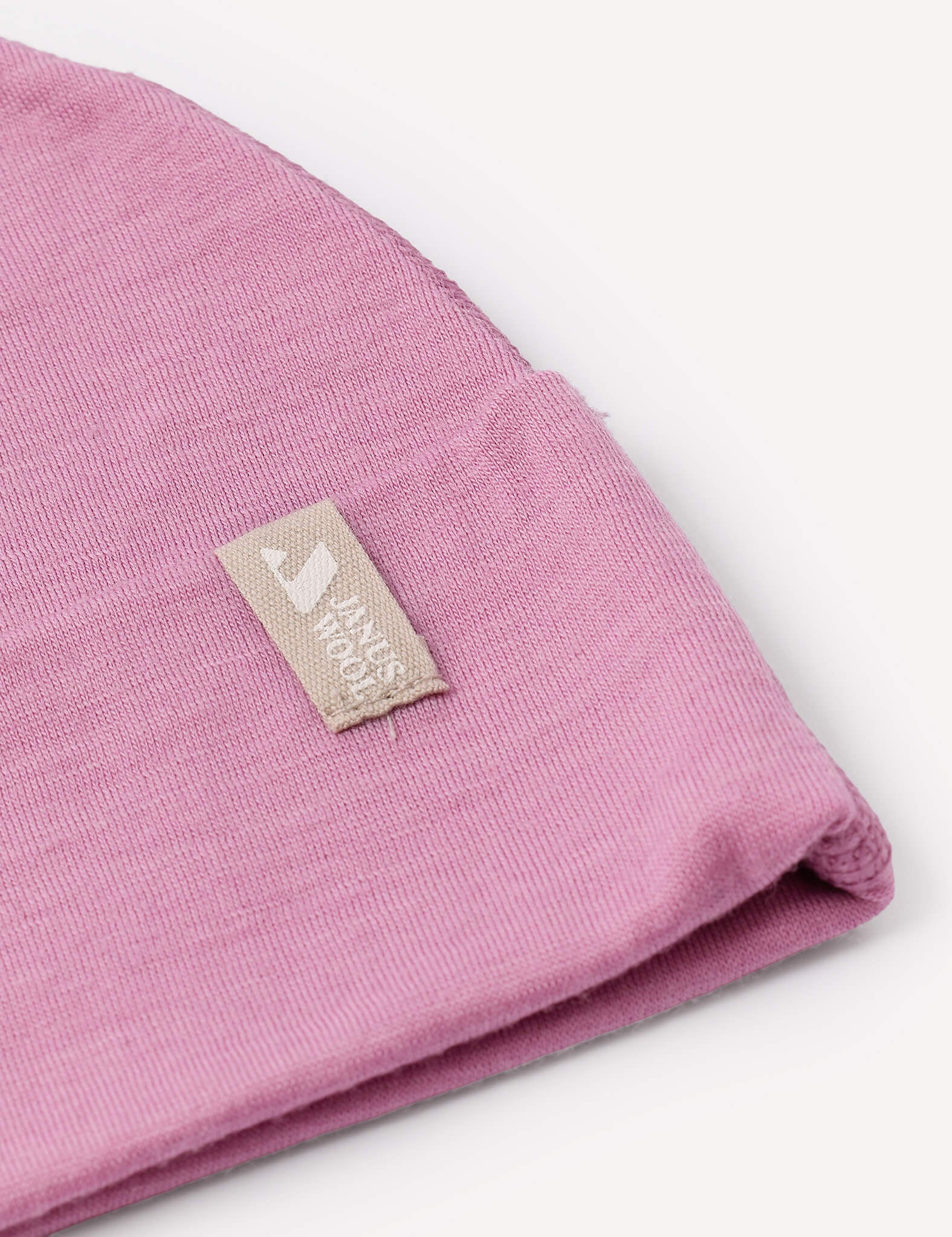 A close-up of a folded pink Beanie – Merino Baby Light hat features a beige label sewn on, displaying a white house icon and the words HOUSE HOOD.
