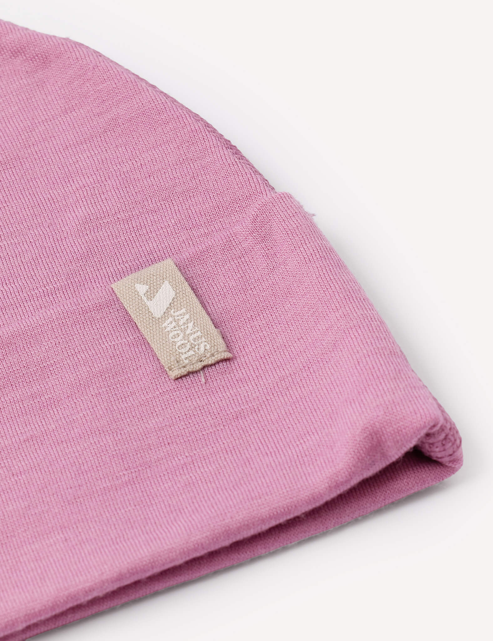 A close-up of a folded pink Beanie – Merino Baby Light hat features a beige label sewn on, displaying a white house icon and the words HOUSE HOOD.