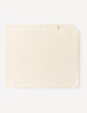 A cream-colored, rectangular Blanket – Merino Baby Light, designed as a lightweight baby blanket with a small tag in one corner, is laid flat on a white background.