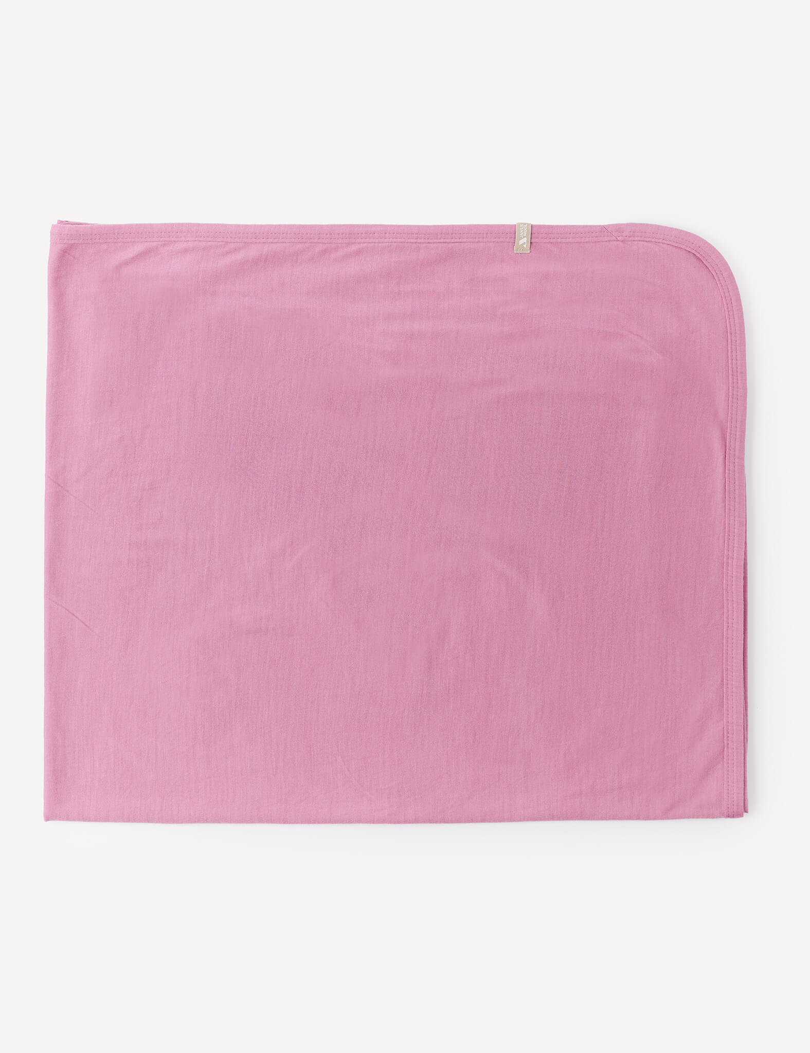 A folded, rectangular Blanket – Merino Baby Light in pink merino wool, featuring a small beige tag on one corner, is displayed on a white background.