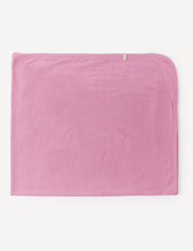 A folded, rectangular Blanket – Merino Baby Light in pink merino wool, featuring a small beige tag on one corner, is displayed on a white background.