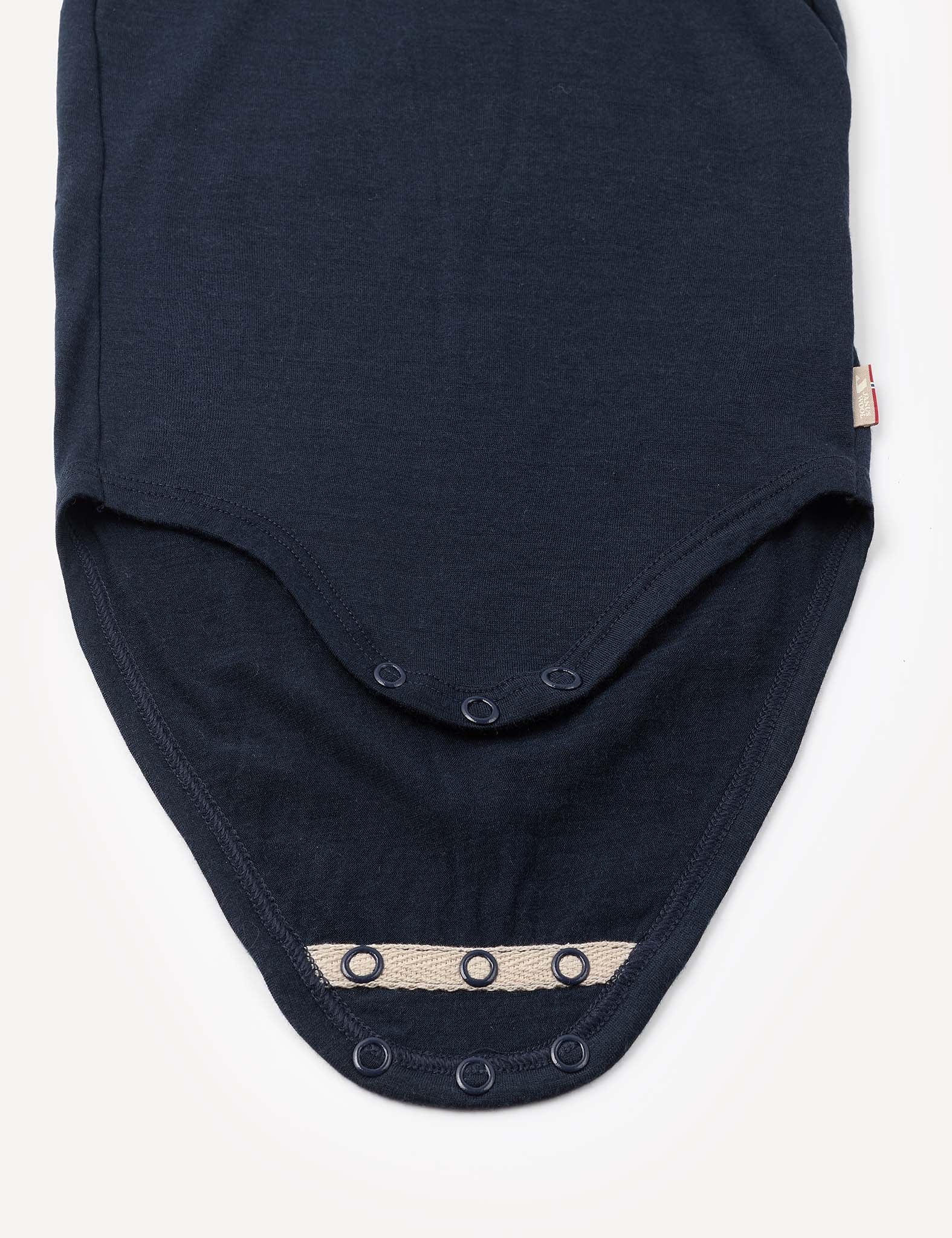 A close-up of the Body – Merino Baby Light, a dark merino wool baby bodysuit featuring snap buttons along two overlapping flaps, laid flat on a white background.