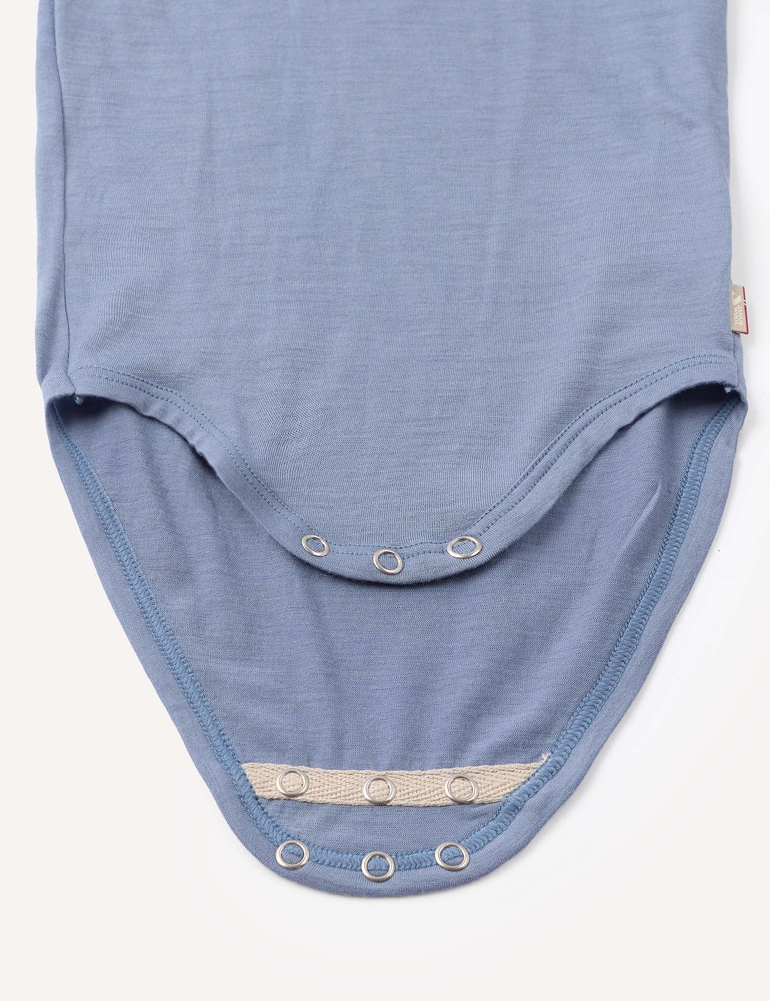 A close-up of the Body – Merino Baby Light, a blue baby bodysuit crafted from soft, breathable merino fabric, featuring metal snap buttons along the curved edges for secure bottom closure.