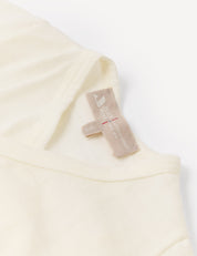 A close-up of a cream-colored shirt’s collar and beige tag, displaying size and care information on a white background, highlights the quality of the Wrapover Bodysuit – Merino Baby Light.