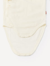 Close-up of the Wrapover Bodysuit – Merino Baby Light in a cream shade, showcasing the bottom half with snap buttons along the edges and at the crotch for easy fastening. The merino wool fabric appears soft, breathable, and lightweight.