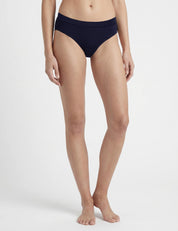A person stands barefoot against a white background, wearing Navy Briefs – Classic Merino 160 Women. The image is cropped from waist to feet, with arms naturally at their sides.