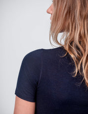 A woman with wavy light brown hair, seen from behind and slightly turned away, models the T-shirt Active – Classic Merino 160 Women in dark navy against a plain light background.