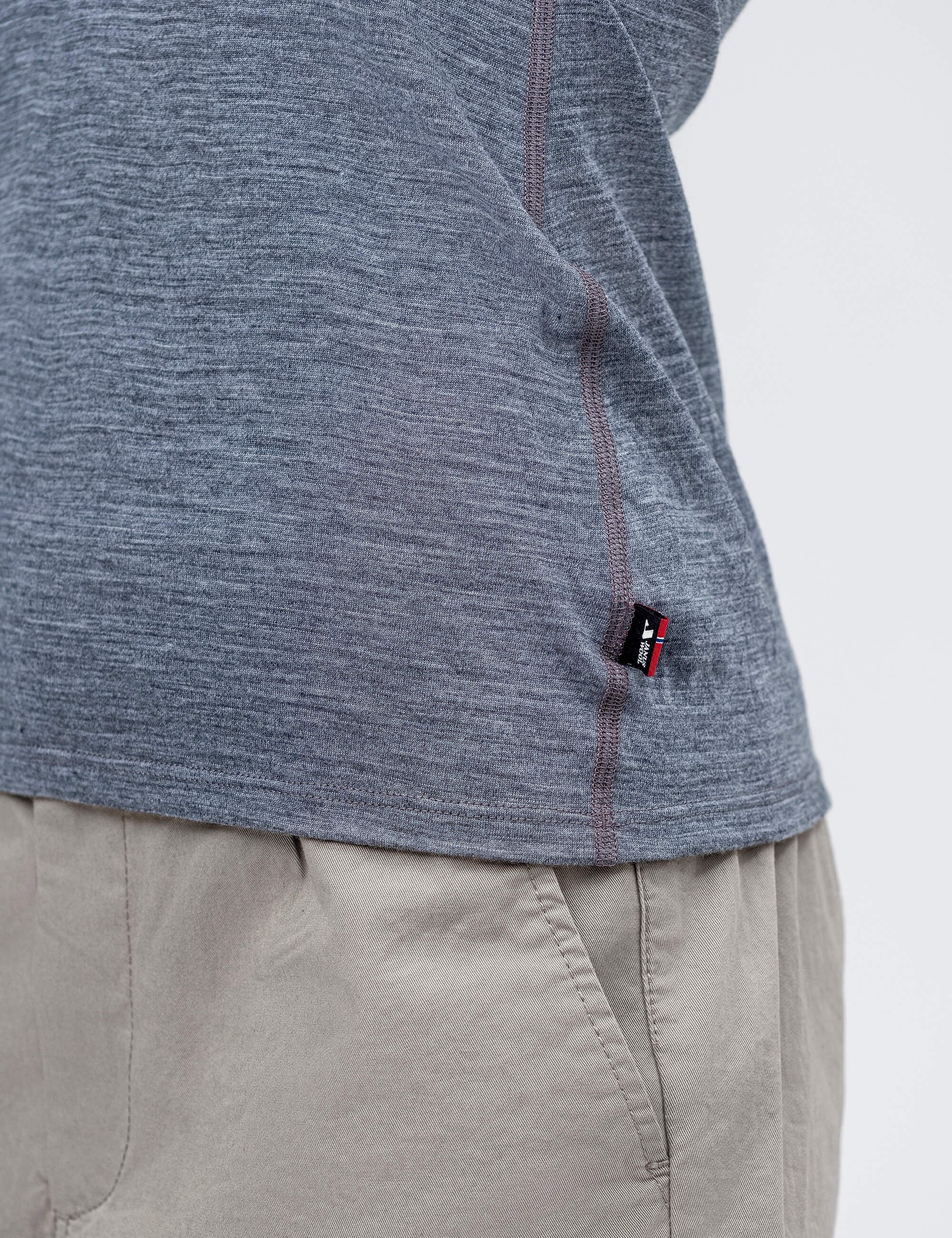 A close-up of a person in the T-shirt Active – Classic Merino 160 Women in heathered gray with a small black tag, paired with beige pants, showcasing the side seam and part of the shirt's hem.