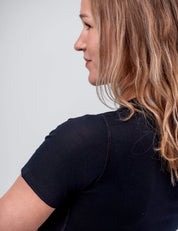 A woman with wavy, light brown hair in profile wears the T-shirt Active – Classic Merino 160 Women for temperature regulation, standing against a plain light gray background.