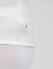 Close-up of the side seam of the Crew Neck – Classic Merino 160 Women t-shirt in white, featuring a small red and white tag. Set against a minimal all-white background for a clean, everyday style.