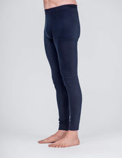 A person models the Leggings – Classic Merino 160 Men in navy blue, showing the lower torso and legs. These form-fitting merino leggings are breathable and temperature regulating, modeled barefoot against a plain light gray background.
