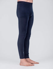 A person stands barefoot on a light gray surface, shown from the waist down in a side view, wearing dark blue, fitted Leggings – Classic Merino 160 Men known for their breathable and temperature regulating properties.