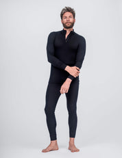 A man with short hair and a beard poses barefoot against a plain light background, wearing fitted, long-sleeve black thermal top with zip collar and Classic Merino 160 Men leggings in black.
