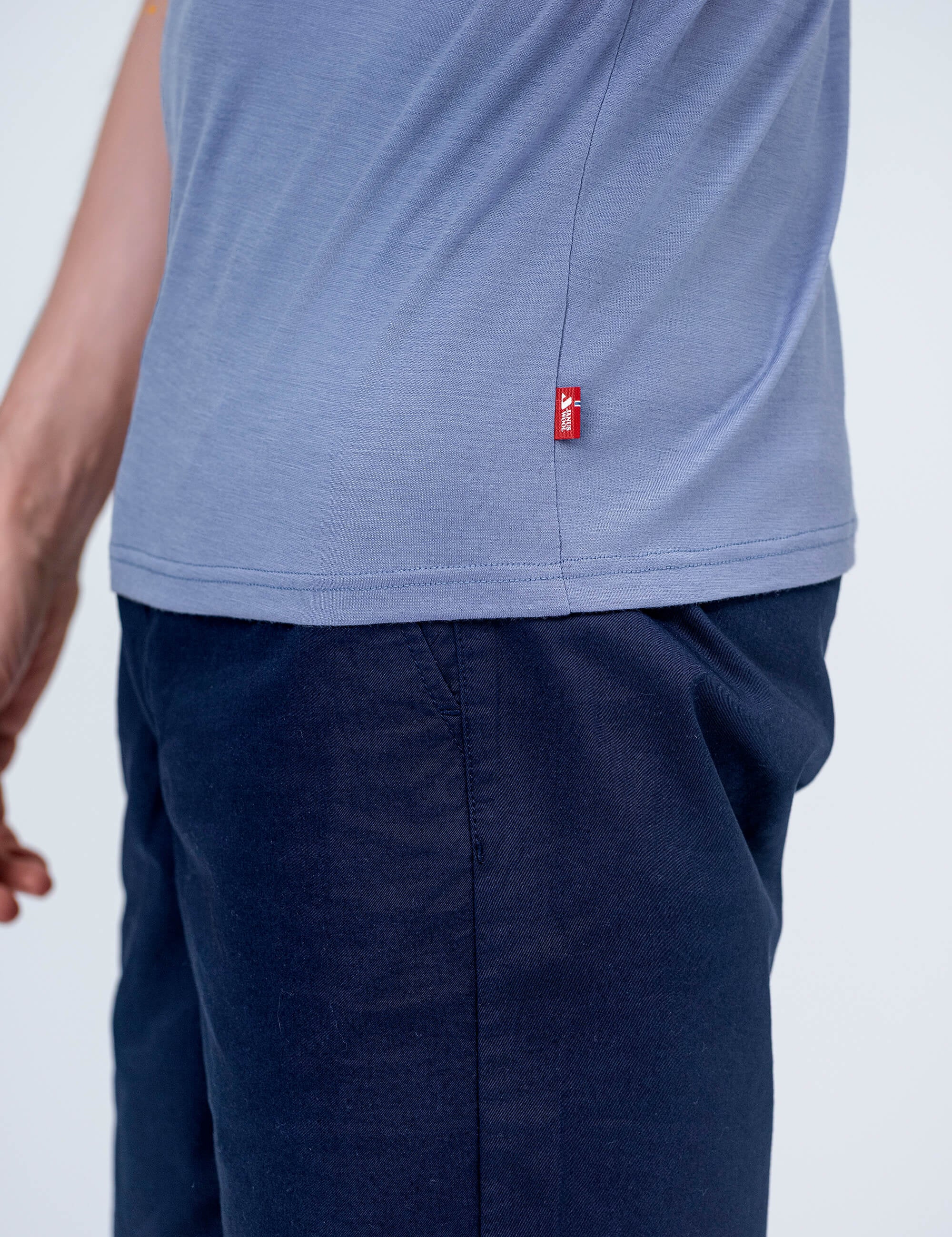 A person wearing the T-shirt Regular – Classic Merino 160 Men in light purple with a small red side tag and dark blue pants, shown from the waist down; their left arm is partially visible.