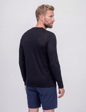 A man with short blond hair and a beard stands facing away, wearing the Crew Neck – Classic Merino 160 Men in black and navy blue shorts, set against a plain light background.