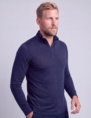 A man with blond hair and a beard is wearing the Half Zip – Classic Merino 160 Men in navy blue along with dark pants, standing against a plain light gray background.