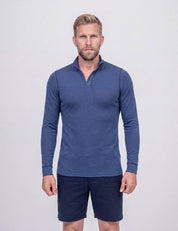 A man wearing the Half Zip – Classic Merino 160 Men in blue and navy shorts stands in front of a plain light-gray background, facing forward with a neutral expression.