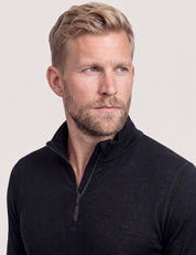 A man with short blond hair and a beard, wearing the Half Zip – Classic Merino 160 Men in black, looks slightly to the left against a plain light background.