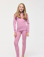A young girl with long, light brown hair stands smiling against a plain white background, wearing a matching light purple Crewneck – Merino Kids Classic Rib wool jersey long-sleeve top and leggings.