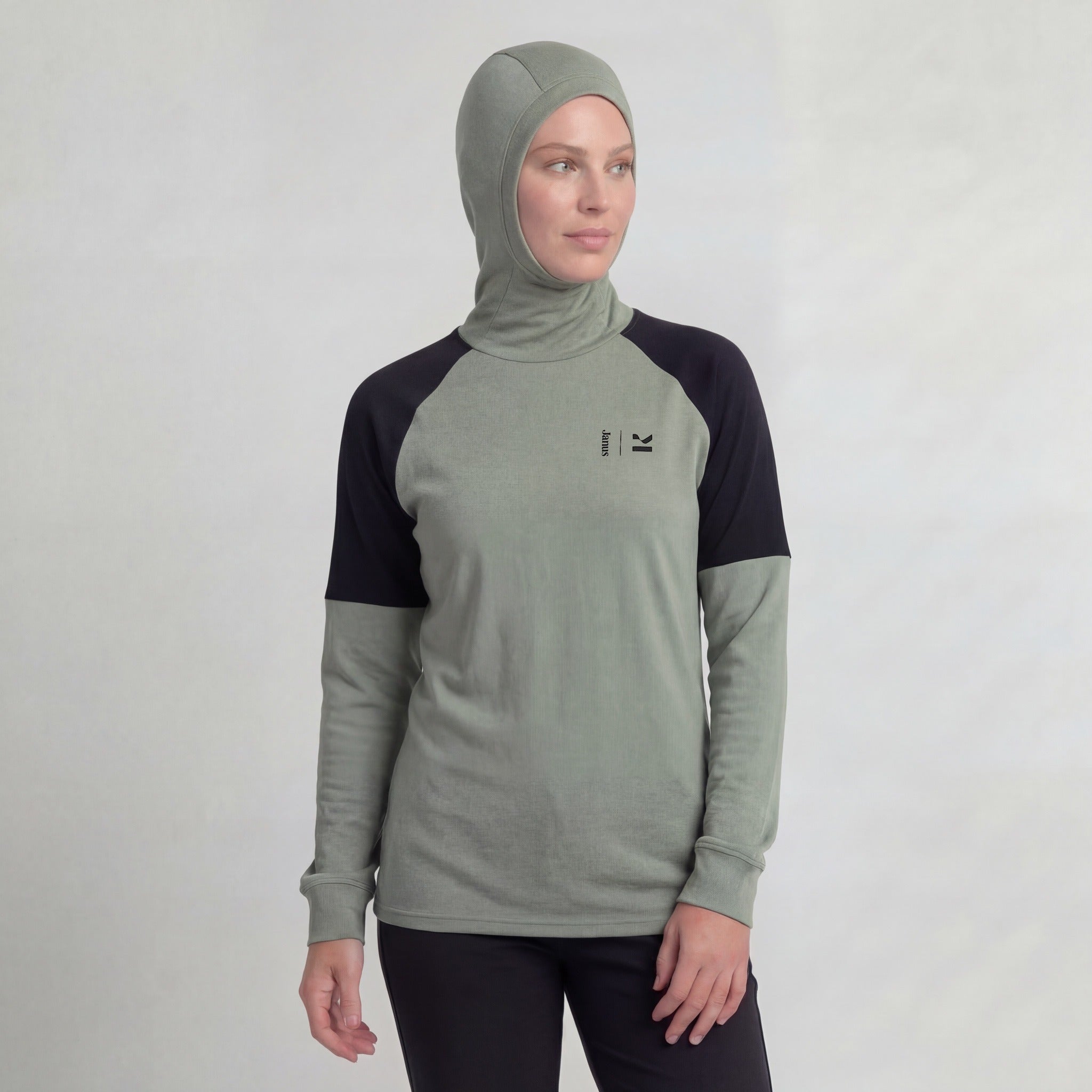 A woman in a green Hooded jersey merino - Kleveland 215 Women stands against a plain background, looking slightly to her left with a neutral expression.