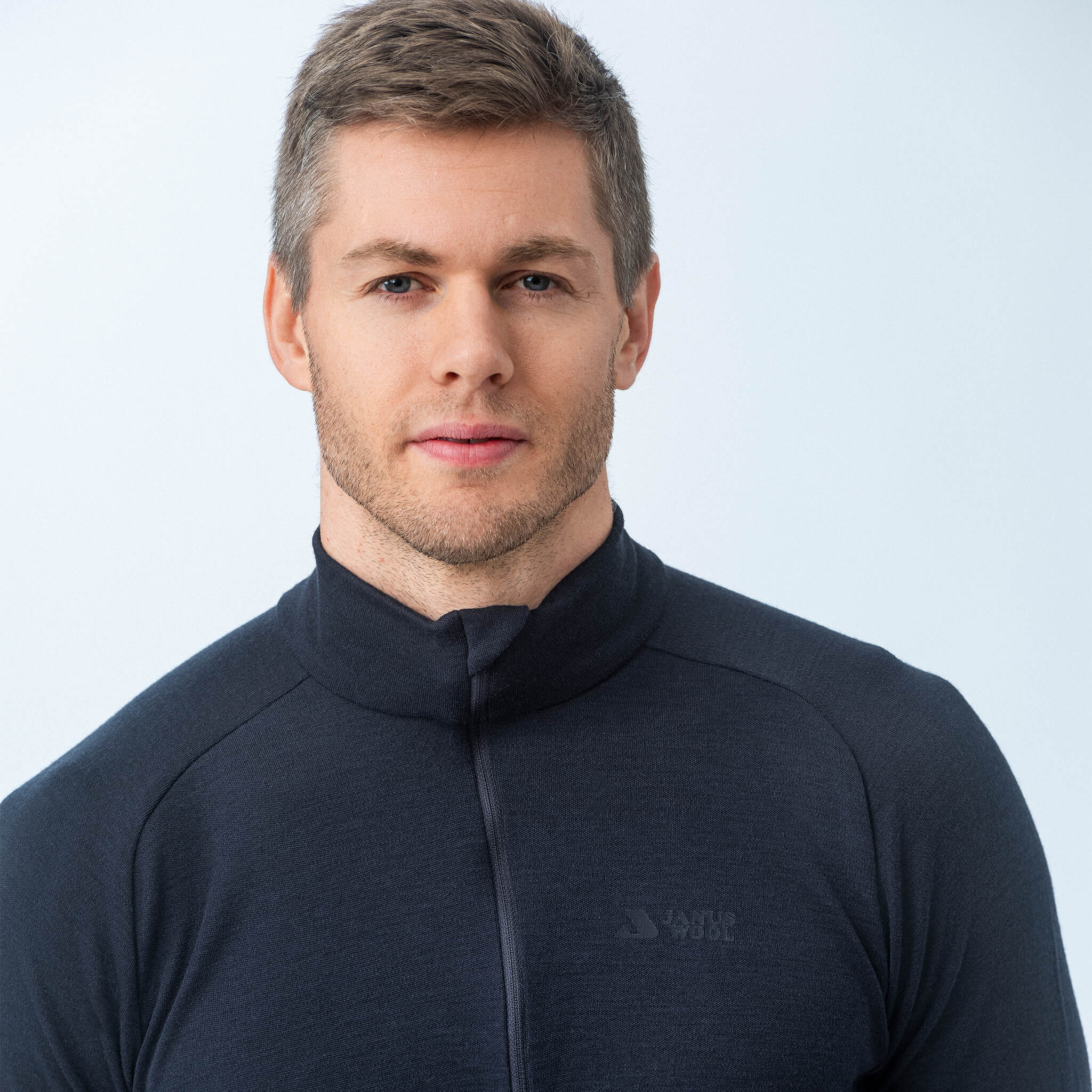 A man with short light brown hair and stubble is wearing the Polo Zip – Classic Merino 215 Men in black, looking at the camera against a plain light background.
