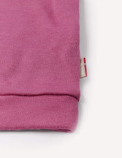Close-up of a pink sleeve from the Pullover – Merino Baby AirWool, featuring a small tag with a red, white, and blue flag detail on the side. Crafted from breathable insulation, this merino wool jumper is set against a white background.