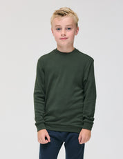 A young boy with short blond hair stands against a plain background, wearing the dark green Pullover – Merino Kids AirWool and navy pants. He is facing forward with a neutral expression.