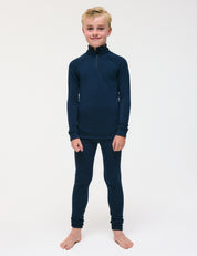 A smiling child with blonde hair wears a navy blue Half Zip – Merino Kids AirWool top and matching leggings, standing barefoot against a plain white background.