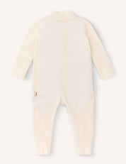 A long-sleeve, cream-colored Onesie – Merino Baby AirWool made from breathable insulation is shown laid flat with the back facing up. The onesie features fold-over cuffs at the wrists and ankles, as well as a small side tag.