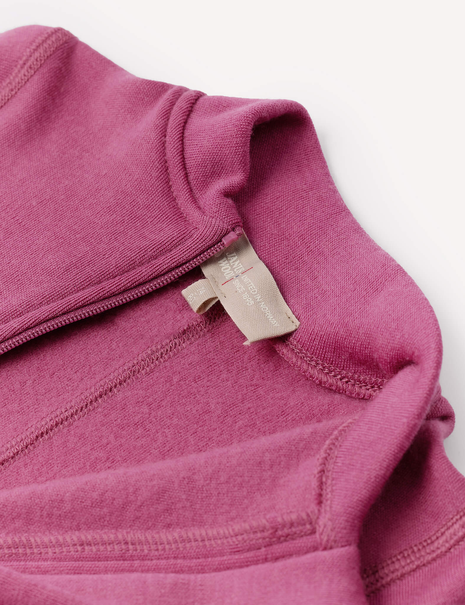 Close-up of the Onesie – Merino Baby AirWool in mauve, highlighting the neckline and inner tag, which is beige with text. The image showcases the fabric texture and stitching details, as well as fold-over cuffs designed for added comfort.