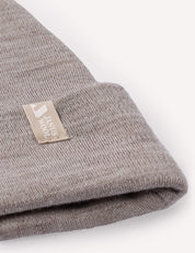 A close-up of a folded, light gray Beanie – Merino Baby AirWool featuring a beige tag that reads KNUS MADE with a small icon beside the text.