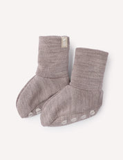 A pair of soft, light brown Booties – Merino Baby AirWool with non-slip white dots on the soles and a small fabric tag on one cuff, displayed on a light background.