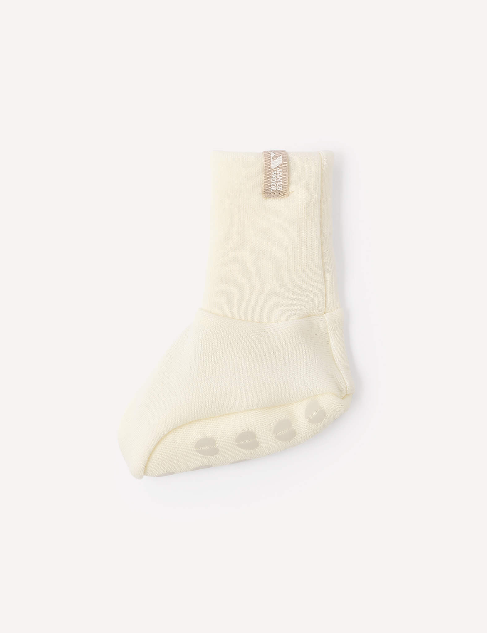 A single Booties – Merino Baby AirWool in a cream color, featuring a beige tag and non-slip grips on the sole, shown on a plain white background.