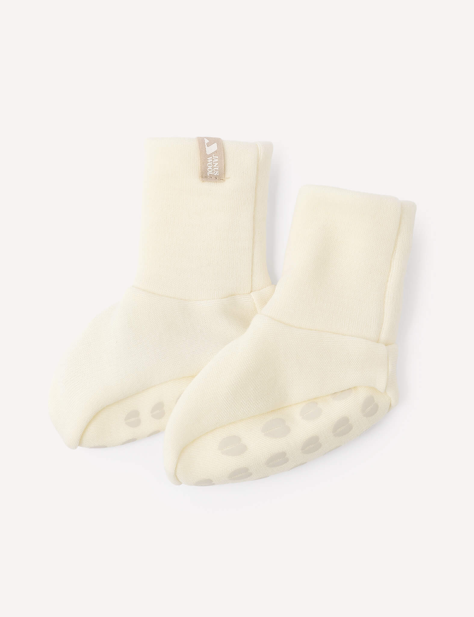 A pair of Booties – Merino Baby AirWool in a cream color, featuring non-slip paw print patterns on the soles, displayed on a white background.
