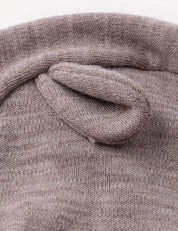 A close-up of the Balaclava – Merino Baby AirWool, a knitted brown hat featuring a small, soft, rounded ear sewn on top to resemble an animal ear, designed as breathable headwear, shown against a plain background.